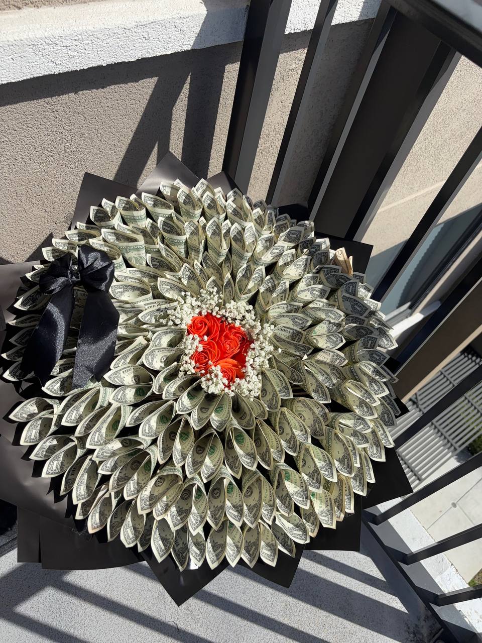 Round money bouquet of folded dollar bills around orange roses and baby's breath, in black wrapping with a black bow