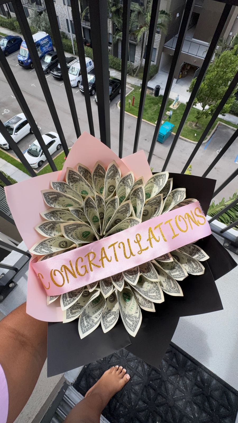 Dollar-bill flower bouquet with a pink sash reading Congratulations, in pink and black wrapping